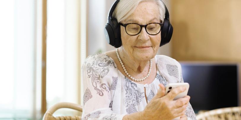 Ikääntynyt nainen älypuhelin kädessä ja kuulokkeet päässä.